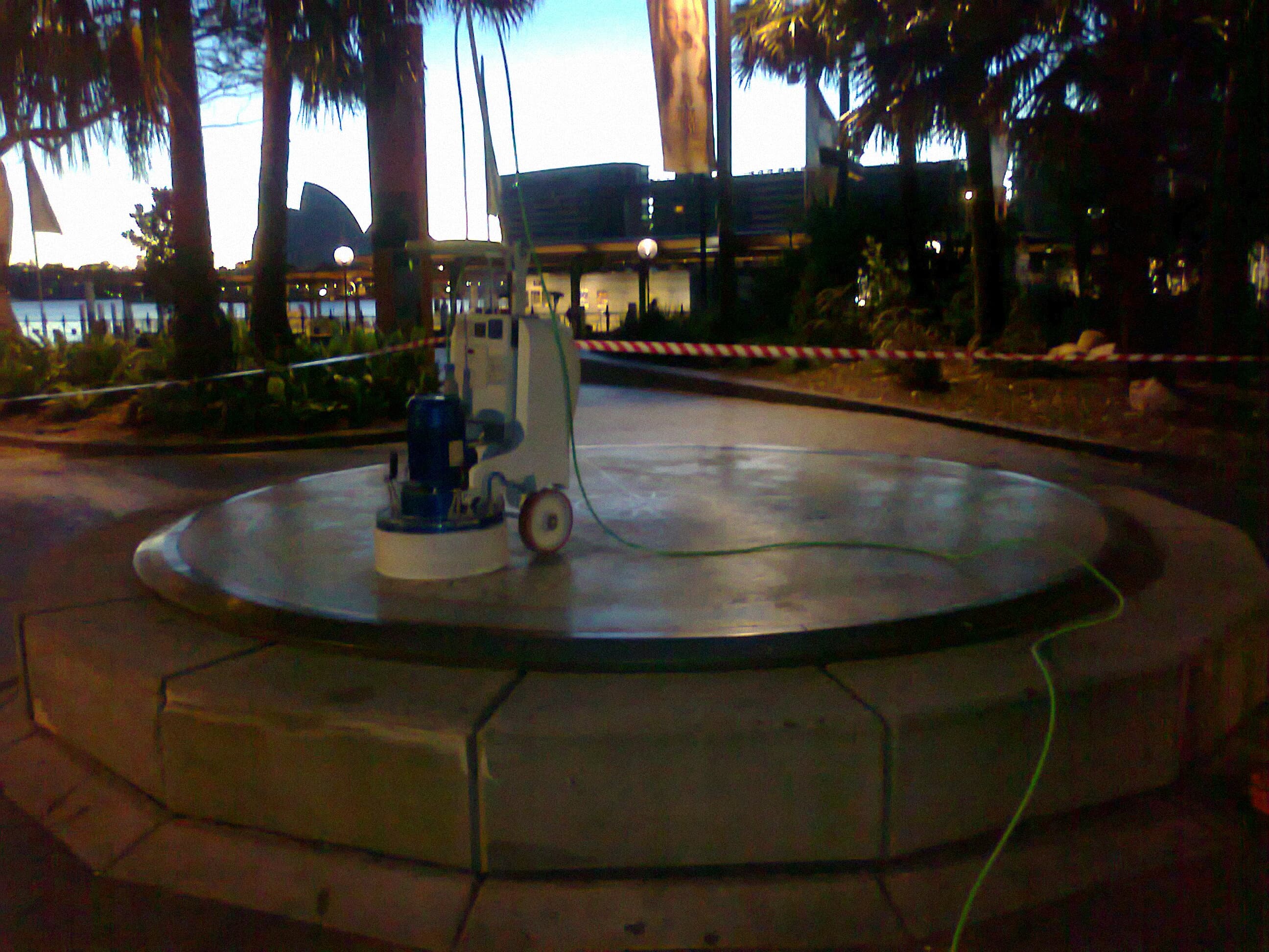 Restoration machine standing on the Sydney Cove 1808 Map inside a taped-off work area at dusk, with the Sydney Opera House visible in the background