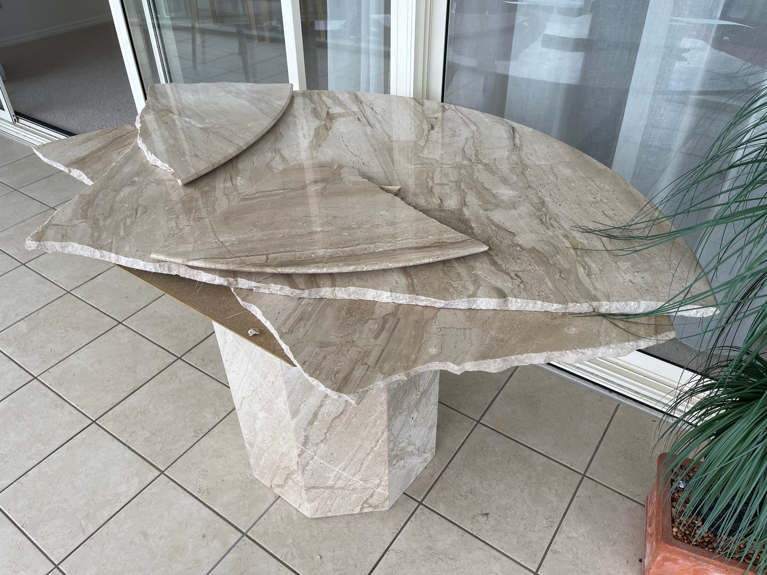 Cracked round natural stone table top lifted unevenly off its pedestal beside a window