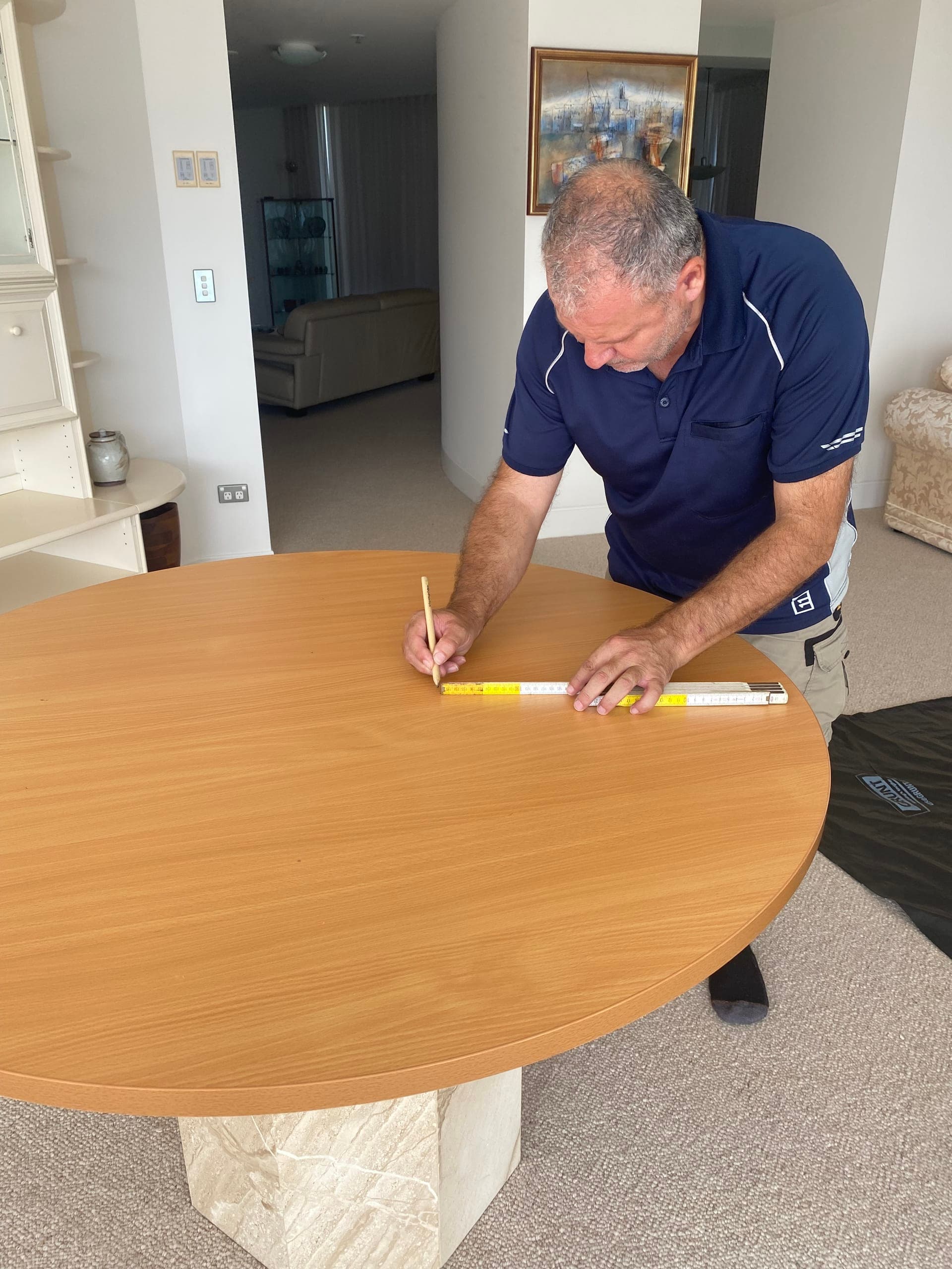 Technician marking measurements across the round timber base top with a straightedge