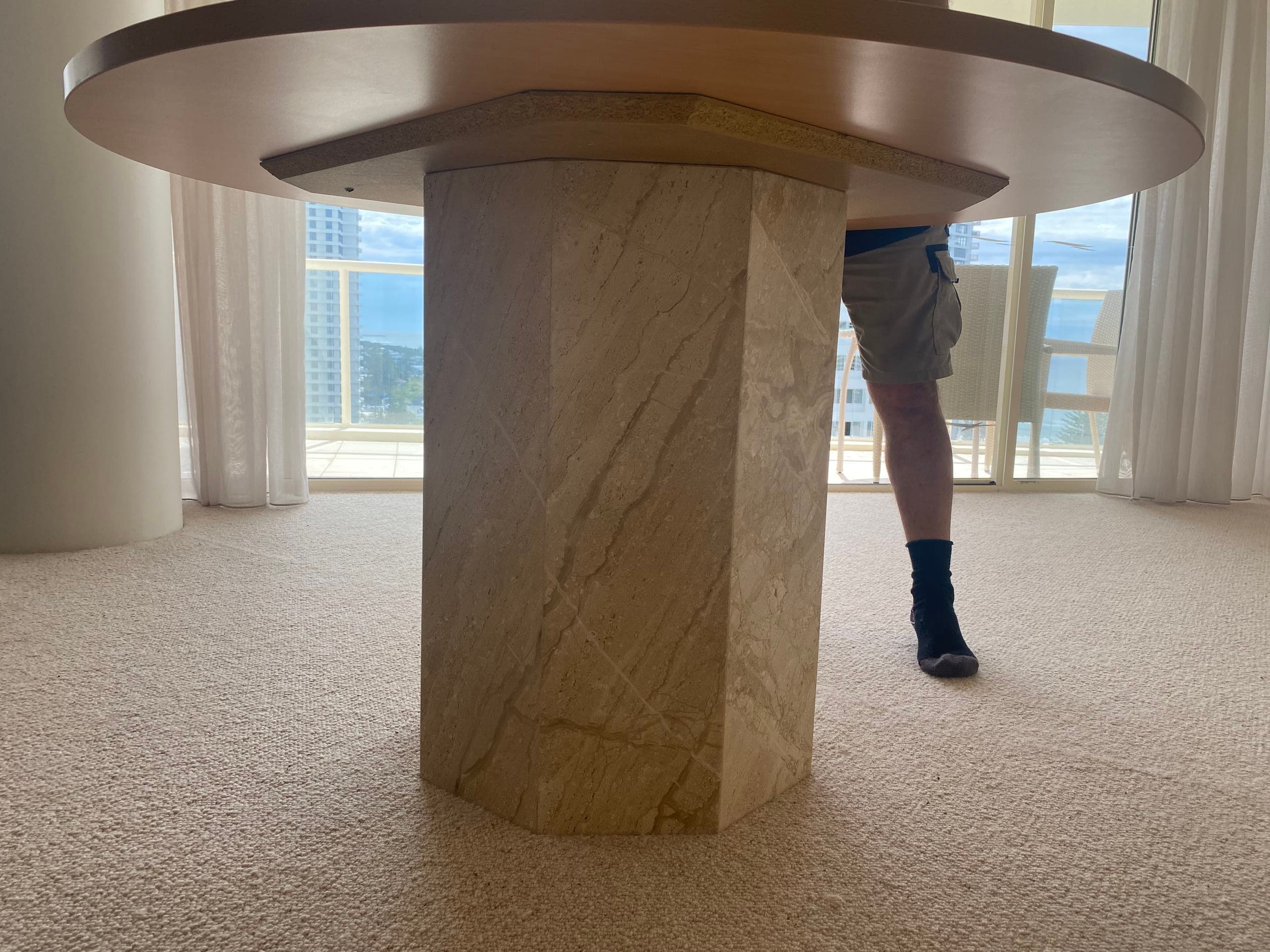 Round timber top on the stone pedestal in an empty room with a water view