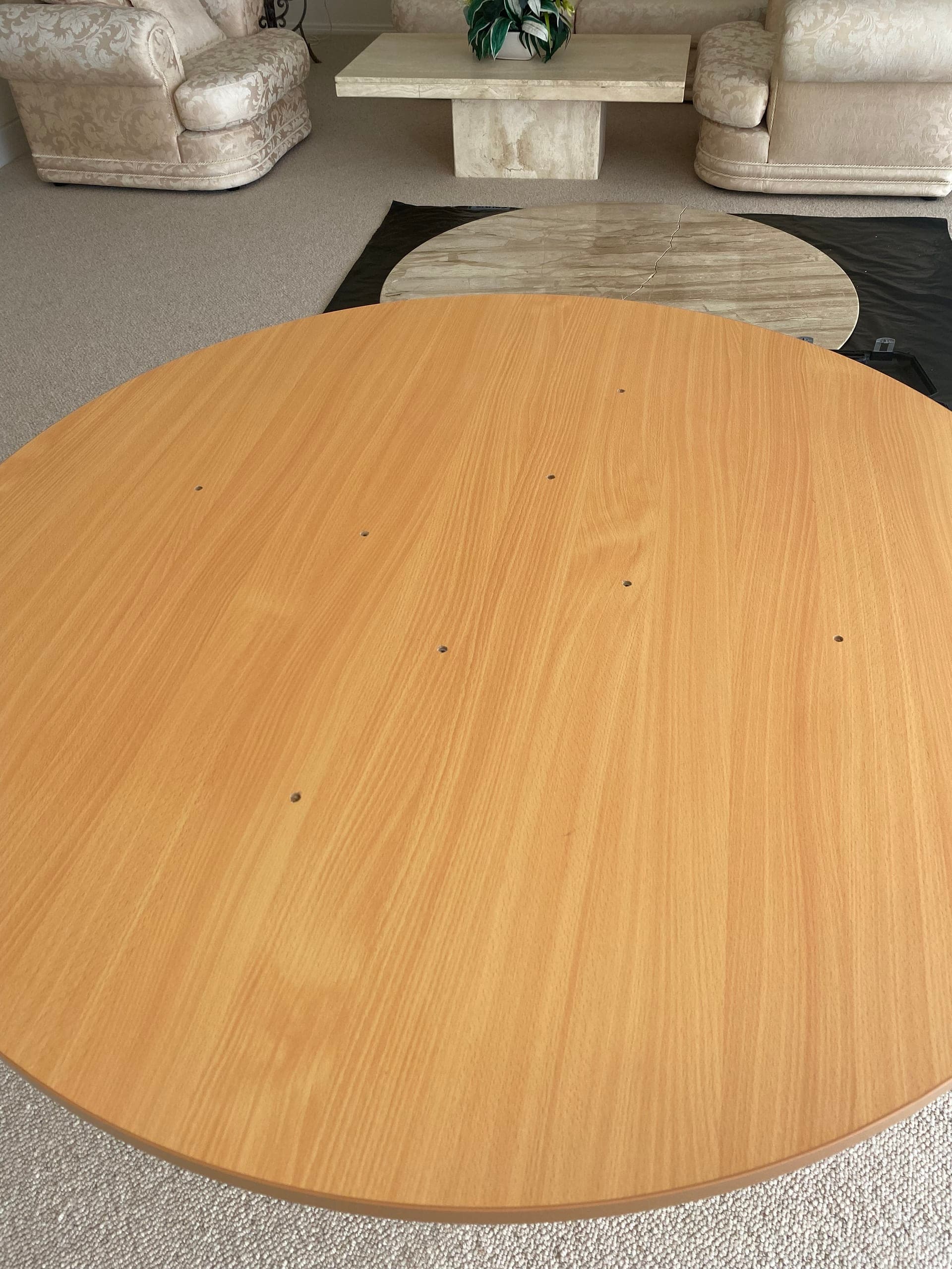 Round timber top standing on carpet with pale lounges behind it
