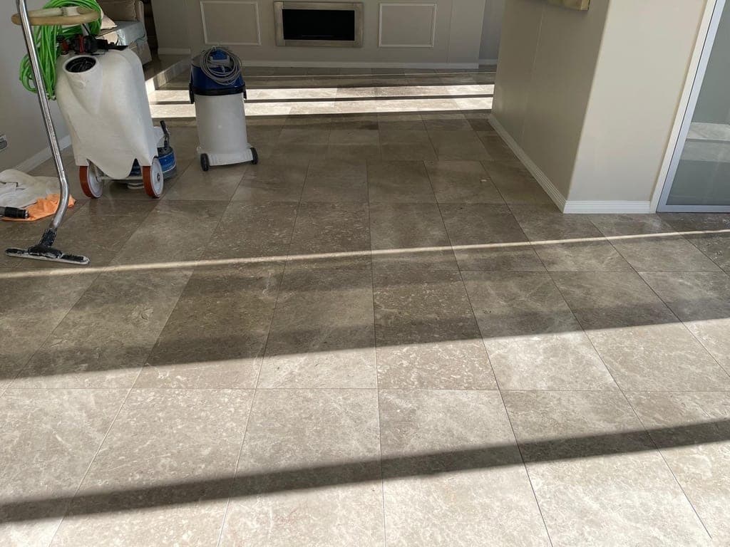 Living-area marble floor before works, with a grinding machine and vacuum set up at the edge of the room
