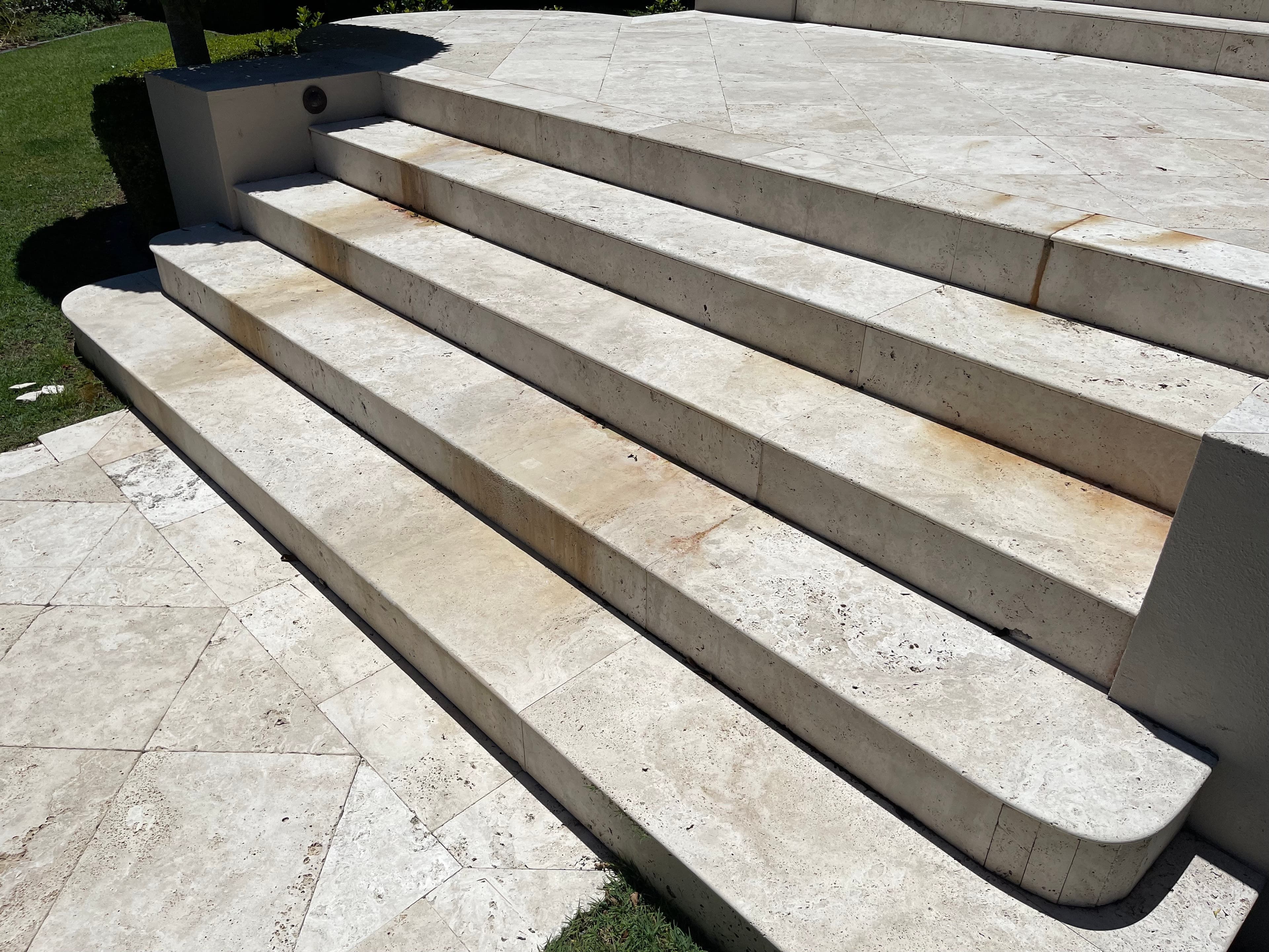 Natural travertine entrance stairs before restoration, with orange-brown staining across the treads and risers